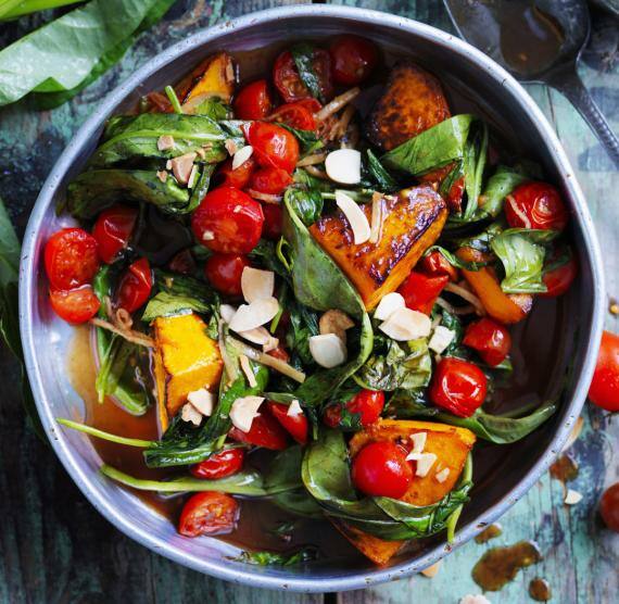 Pfanne mit Kürbis, Spinat, Tomaten und Mandeblättern in dunkler, dünner Sauce