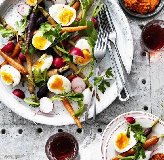 Weißer Teller mit gebratenen Karotten, Eierhälften, Radieschenscheiben und Petersilie, daneben Schälchen mit Dip 