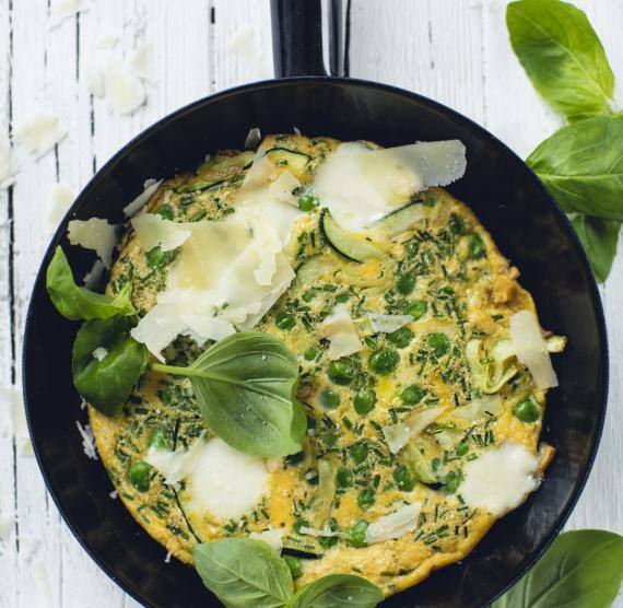 Pfanne mit Frittata mit Erbsen und Zucchini, darauf Parmesanspäne, Basilikum und Schnittlauch
