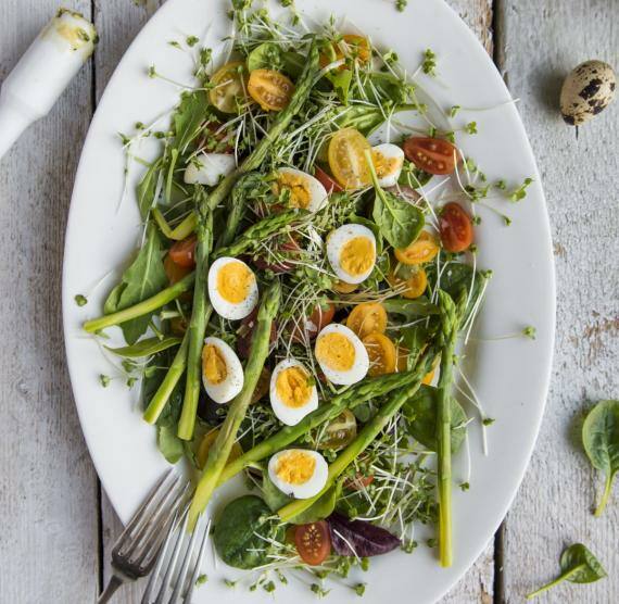 Ovaler Teller mit Spargel, Kirschtomaten, halbierten Wachteleiern, Salat und Pesto