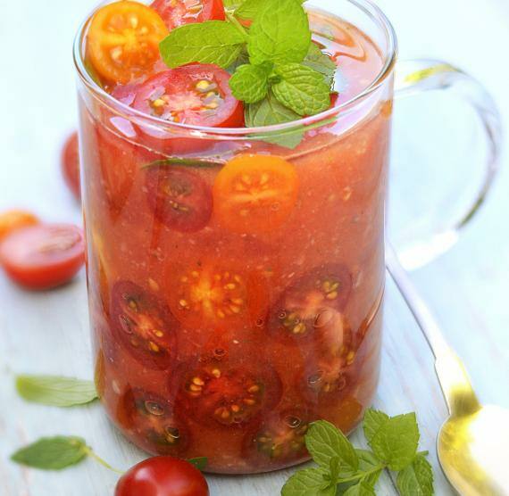 Glastasse mit Tomatensuppe und halbierten Kirschtomaten, daneben und darauf Minze