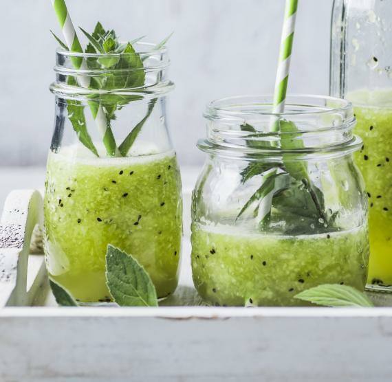 grüner Smoothie in Gläsern und Flasche, in den Gläsern sind Strohhalme und dekorative Minze