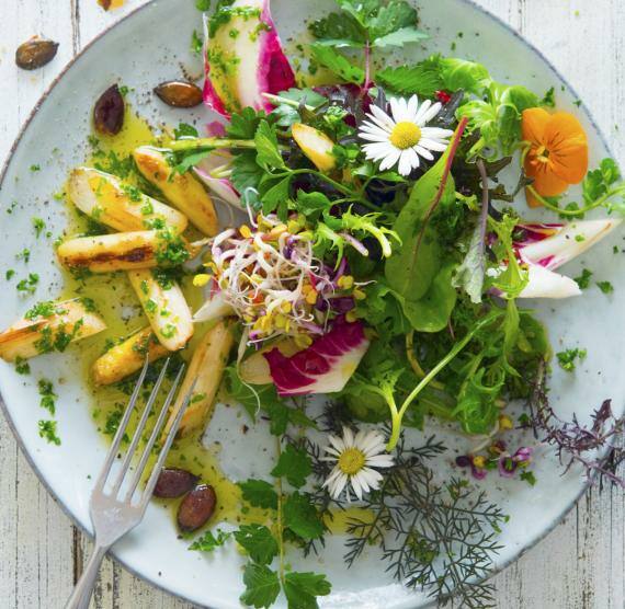 Spargelsalat mit Essblüten auf Teller und kleine Schale Dressing