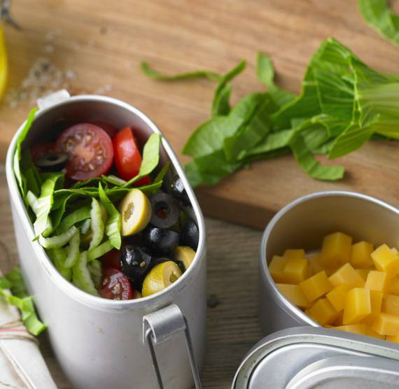 Tomaten-Oliven-Salat mit Pak Choi in Metalldosen vor einem Holzbrett