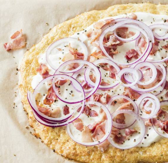 Flammkuchen mit Blumenkohlboden auf einem Brett mit Backpapier