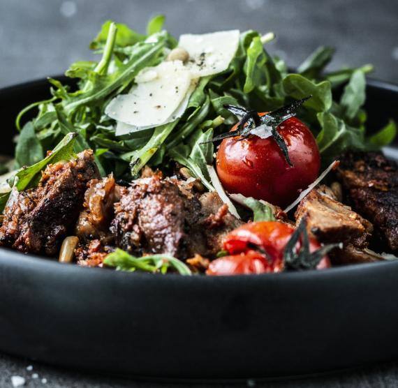 Steak mit Ofentomaten, Parmesan und Rucola in einer dunklen Schüssel