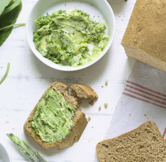 Brotscheibe mit Bärlauchbutter neben Brotlaib und Butterschälchen