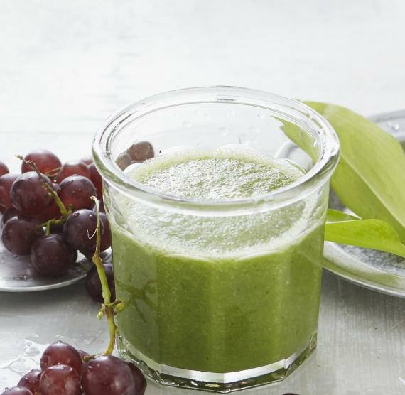 Grüner Smoothie im Glas neben Weintrauben und Gurkenscheiben