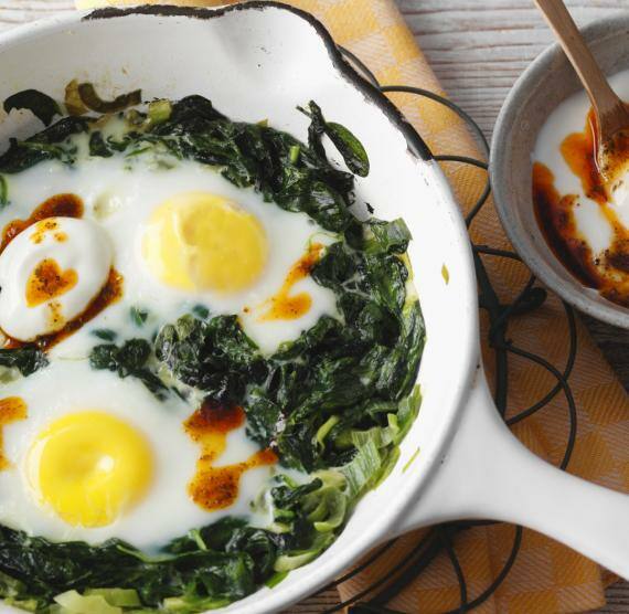 Spinat-Spiegelei-Gericht in Pfanne mit Joghurt in Schüsselchen.