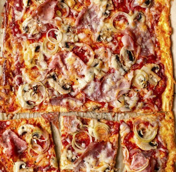 Pizza mit Pilzen, Schinken und Zwiebeln auf Backpapier