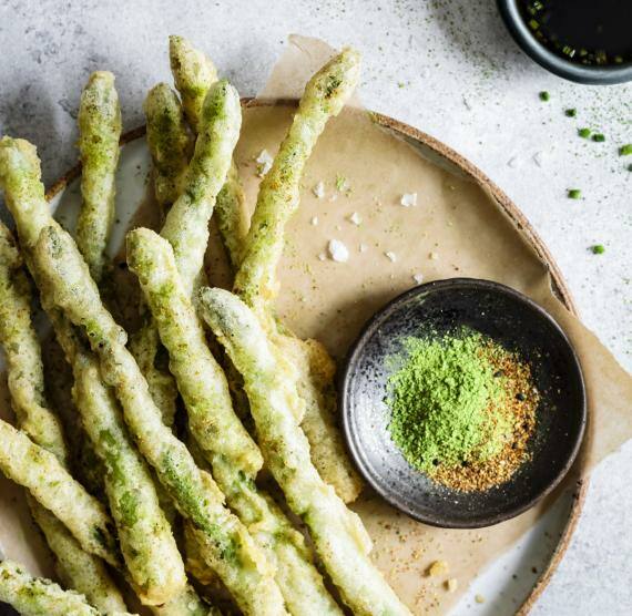 Teller mit Backpapier und Tempura-Spargel und Schalen