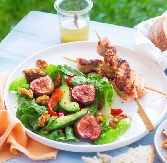Teller mit Salat,Feigen und Lachsspießen auf einem Tisch ,Dressing im Glas