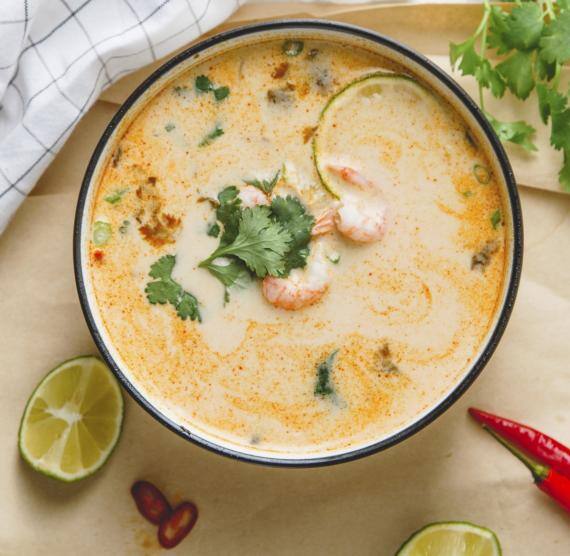 Schale mit Suppe auf Brett, daneben Limette, Chili und Koriander