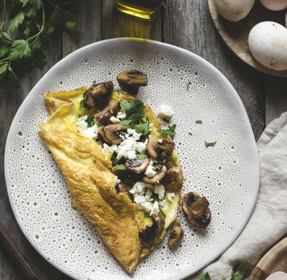 Omelett mit Pilzen und Feta auf einem Teller mit Eiern und Olivenöl