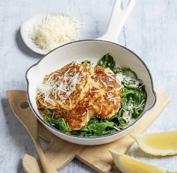 Pfanne auf einem Holzbrett mit Puffern und Spinat