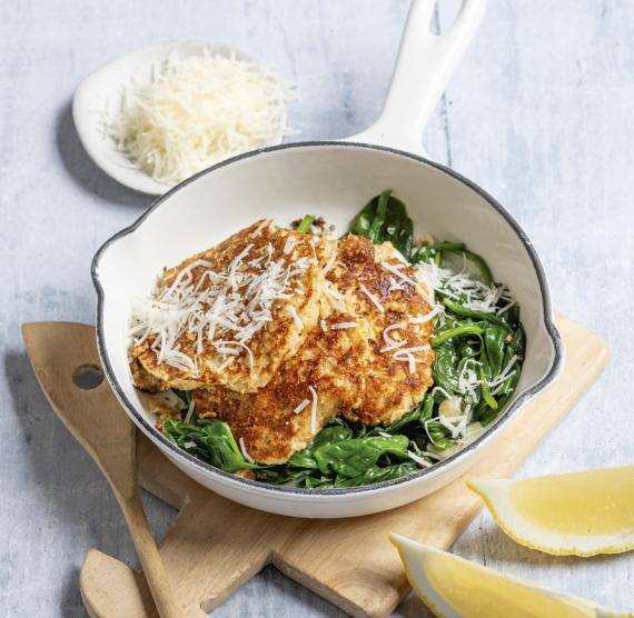 Pfanne auf einem Holzbrett mit Puffern und Spinat