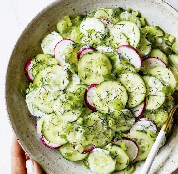 Gurkensalat in einer Schüssel mit zwei Händen und Löffel