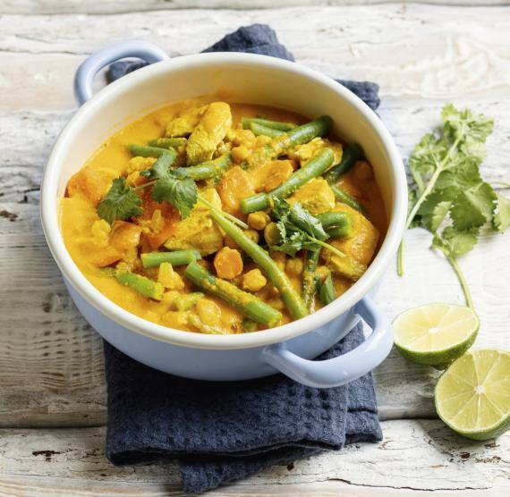 Curry in einem Topf mit Koriander und Limetten daneben