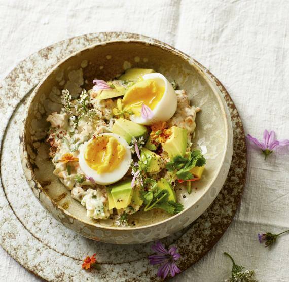 Schale mit Eiersalat und halbiertem Ei auf Brett mit Blüten