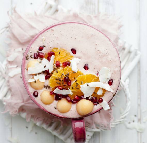 Becher auf einem Tuch mit Orangen,Kokosraspeln, Granatapfel und Melone