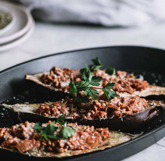 Schwarze Pfanne mit drei Auberginenhälften, gefüllt mit Bolognesesauce, darüber Petersilie