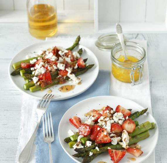 Zwei Teller mit grünem Spargel, Erdbeeren, Feta und Sauce