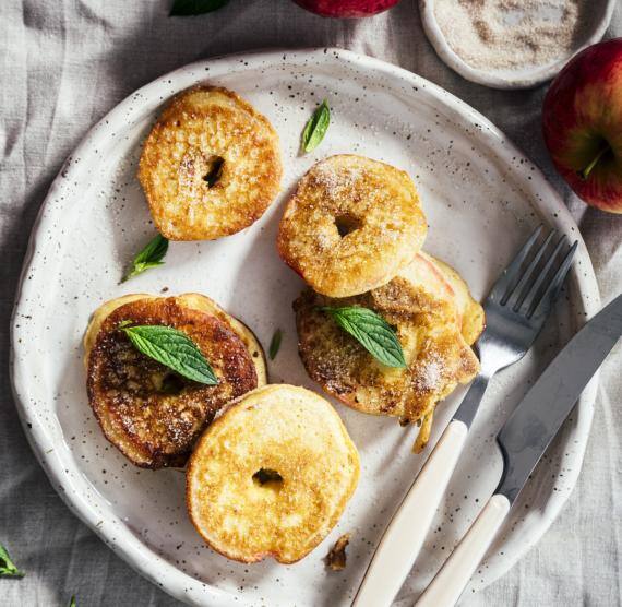 Heller Teller mit fünf frittierten Apfelringen im Pfannkuchenmantel, darauf grüne Blätter