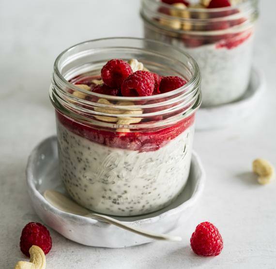 Gläschen mit Chiapudding, Himbeercreme, Himbeeren und gehackten Cashewkernen