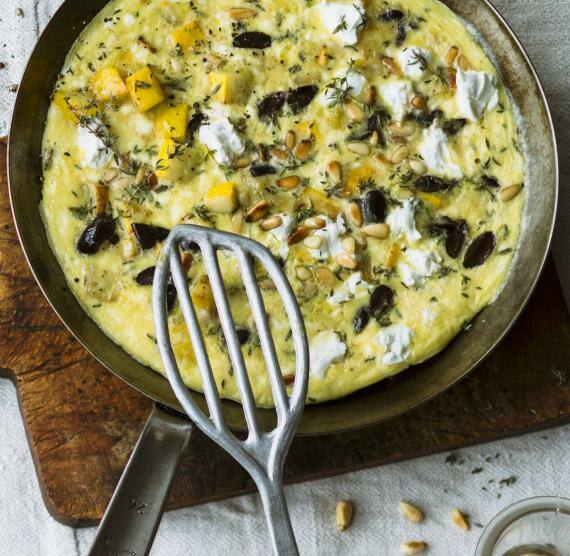 Pfanne auf Brett mit Omelett mit Zucchini, Oliven, Feta, Pinienkernen und Thymian