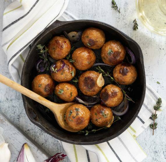 Pfanne mit veganen Hackbällchen, roten Zwiebeln, Knoblauch und Thymian, daneben frischer Knoblauch, frische Zwiebeln