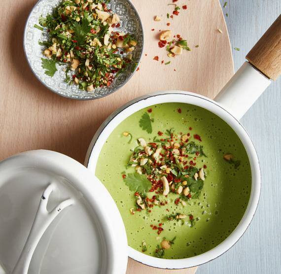 Topf mit grüner Suppe und Topping aus Petersilie, Cashews und Chiliflocken, daneben Schälchen mit mehr Topping
