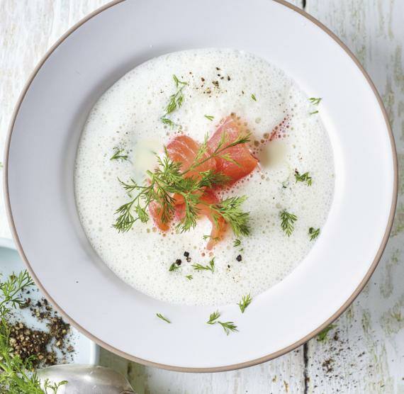 Suppe mit Räucherlachs in einer hellen Schüssel, daneben Kräuter