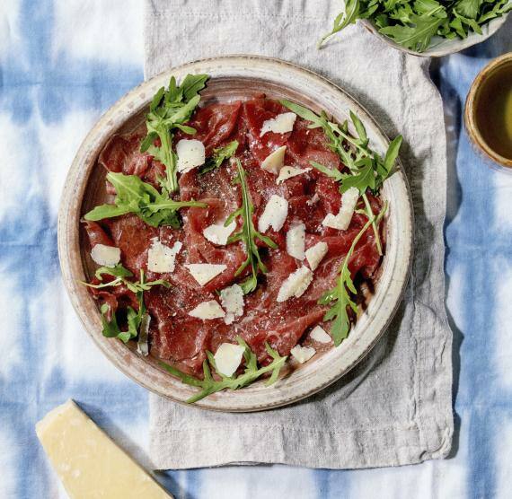 Carpaccio-Teller mit Rucola auf blauer Tischdecke