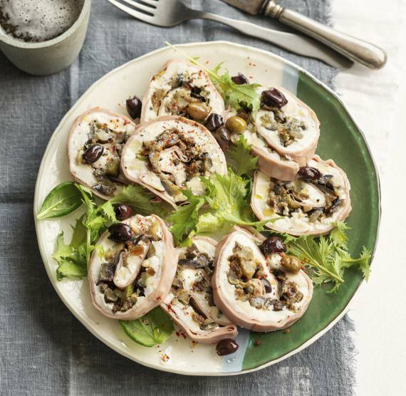 Mortadella Rouladen auf grün-weißem Teller mit Oliven und Salat 