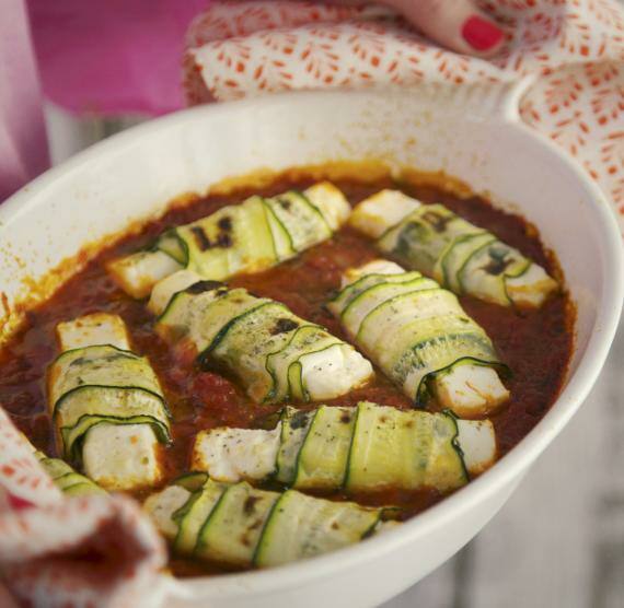 Helle Auflaufform mit Zucchini-Feta-Röllchen in Tomatensauce
