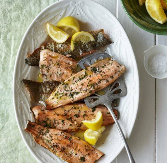 Weißer Teller mit gegrillten Forellenfilets mit Kräutern und Zitronenspalten