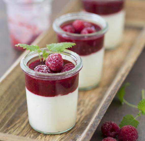 Gläschen mit Joghurt und Himpeerpüree, darüber frische Himbeeren und Zitronenmelisse