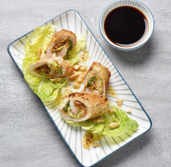 Auf Salatblättern angerichtete Putenröllchen mit Erdnusscremefüllung, daneben ein Schälchen mit Sojasauce