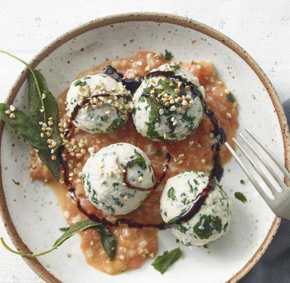 Teller mit 3 Ricotta-Gnudi auf geschmolzenen Tomaten, daneben Salbeiblätter, darauf gerösteter Buchweizen