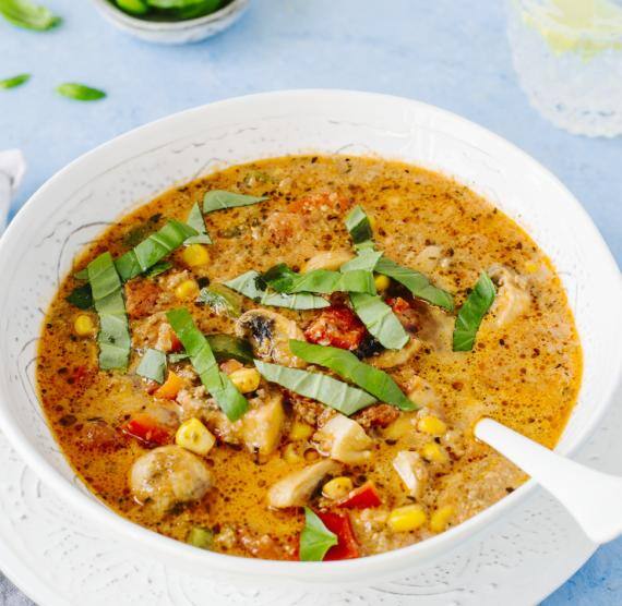 Suppe im Teller mit unter Teller, Schale mit Basilikum und Glas Wasser