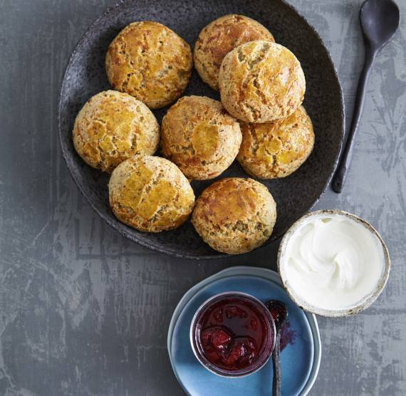 Schwarzer Teller mit 8 Scones, daneben Löffel, Schälchen mit Saurer Sahne und Marmelade