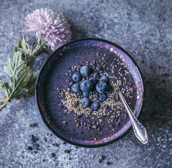 Schüssel mit lila-farbener Smoothie, darüber Beeren, Kakao Nibs und Sesam