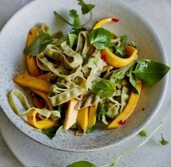 Grüne Nudeln mit Mango und Sauce in einem tiefen Teller