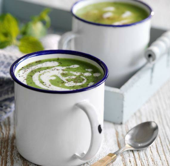 Erbsensuppe in weißen Emaillebechern mit Löffeln