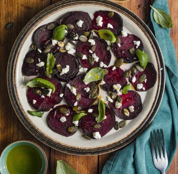 Rote-Bete-Carpaccio auf einem Teller, darüber Basilikum, Feta und Kürbiskerne
