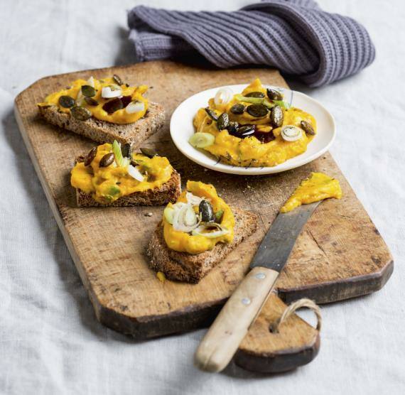 Brett mit Brotscheiben mit Kürbisaufstrich, darüber Kerne und Frühlingszwiebeln