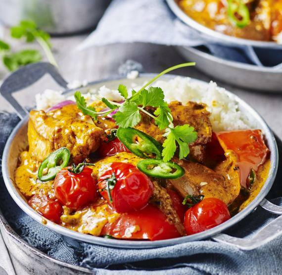 Buntes Curry mit Hähnchen in einer Schale, daneben Blumenkohlreis