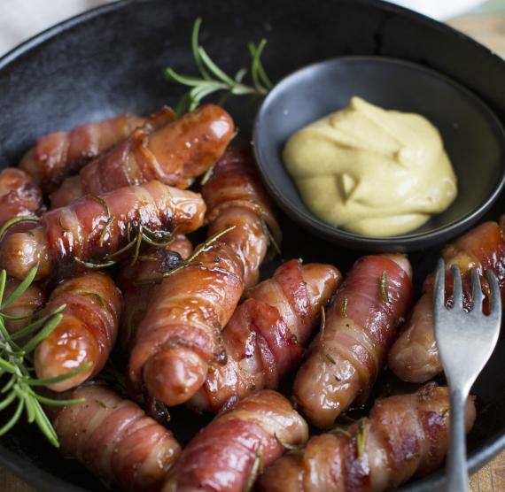 Würstchen im Speckmantel mit Rosmarinzweig und Senf in einer Pfanne