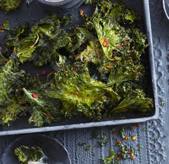 Grünkohlbläter auf einem Blech, daneben Schüsselchen mit Dip