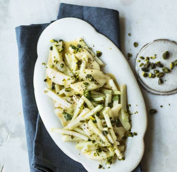 Kohlrabi-Salat auf einem Servierteller, der auf einem blauen Tuch steht, daneben Pistazien